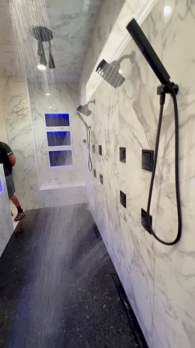 A finished marble shower with multiple matte black shower fixtures under running water.