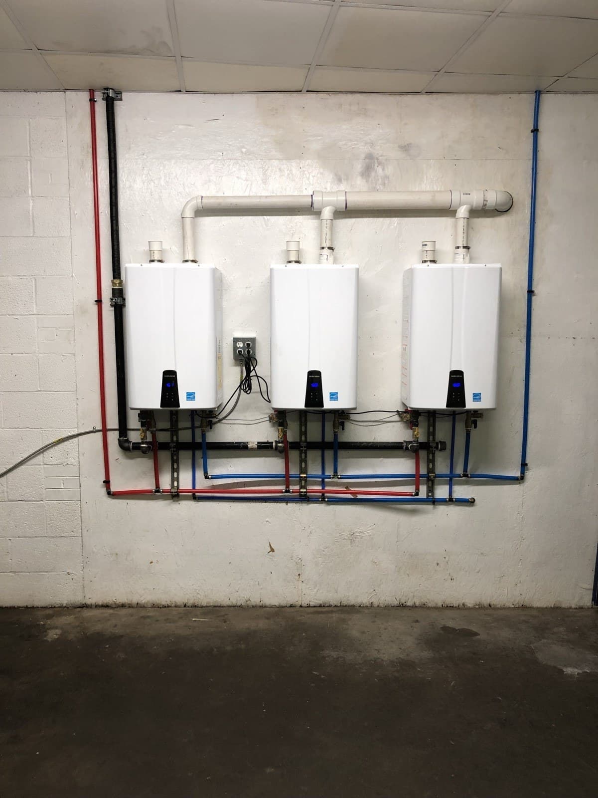 Three wall-mounted tankless water heaters installed on a finished plumbing wall.